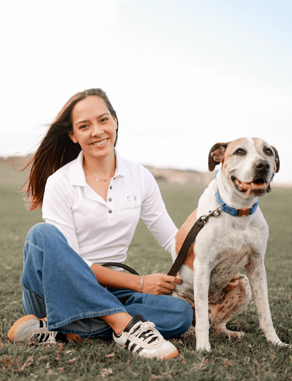 Anayla Fontán Núñez arrodillada en un campo de hierba junto a un golden retriever blanco y feliz, con la torre de un fuerte de Puerto Rico visible a lo lejos